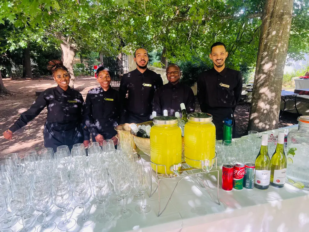 Five staff behind a white-clothed table lined with rows of wine glasses and juice dispensers